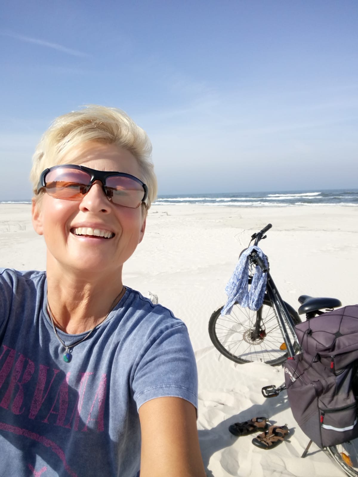 blondynka w krótkich włosach i okularach przeciwsłonecznych szczęśliwa na plaży, w tle rower