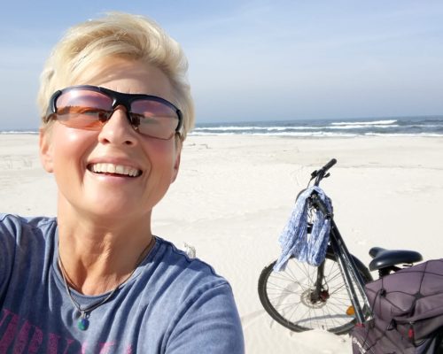 blondynka w krótkich włosach i okularach przeciwsłonecznych szczęśliwa na plaży, w tle rower